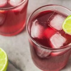 two glasses filled with red liquid and limes