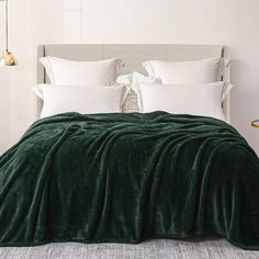 a bed covered in a green blanket next to a night stand with two lamps on it