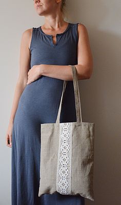 a pregnant woman wearing a blue dress and carrying a beige tote bag with white lace trim