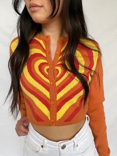 cropped orange cardigan with red, orange, and yellow heart design available in sizes xs, s, m, l model is 5'3" and wearing a size small Fitted Heart Print Sweater For Fall, Orange Fitted Long Sleeve Cardigan, Fitted Orange Long Sleeve Cardigan, Fitted Long Sleeve Orange Cardigan, Retro Orange Cardigan For Winter, Orange Retro Long Sleeve Sweater, Orange Long Sleeve Retro Sweater, Retro Orange Long Sleeve Sweater, Fitted Orange Cardigan For Spring