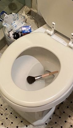 a toilet with the lid up and a brush in it's bowl, sitting on a tiled floor