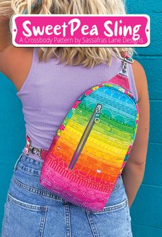 a woman wearing a rainbow colored backpack with the words sweet pea sling on it's back