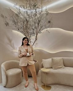 a woman standing in front of a couch with a tree on the wall behind her