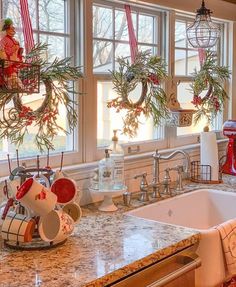 a kitchen decorated for christmas with wreaths on the windowsill and other holiday decorations