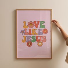 a woman holding up a framed art print with the words love like jesus on it