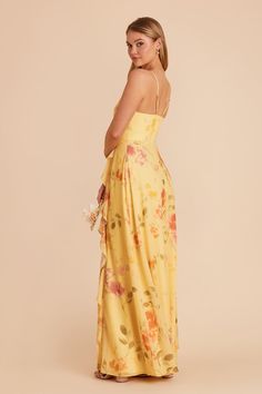 a woman in a yellow floral print dress with her back turned to the camera,