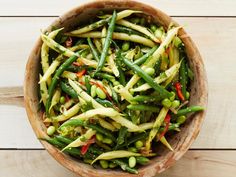 a wooden bowl filled with green beans and other vegetables on top of a wooden table