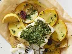 a white plate topped with fish and potatoes covered in pesto sauce next to a fork