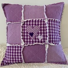 a purple and white checkered pillow with hearts in the center on top of a bed