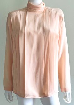 Vintage C1980s pure butter soft silk blouse from Linda Allard For Ellen Tracy in a gorgeous, delicate shade of peach or soft coral, featuring a roll neck, soft front pleats, and a rear self covered buttons closure.  Shoulder pads (removable). Approximate Measurements:      Bust: 39"; Waist: 37"; Hips: 41"; Length: 28"      Labeled a size 6 Fabric: 100% Silk Condition: Elegant C1980s blouse is in excellent vintage condition; with small marks on back, as shown. Feminine Long Sleeve Apricot Blouse, Feminine Peach Long Sleeve Blouse, Feminine Long Sleeve Peach Blouse, Elegant Fitted Peach Blouse, Shades Of Peach, Soft Coral, Ellen Tracy, Roll Neck, Blouse Top