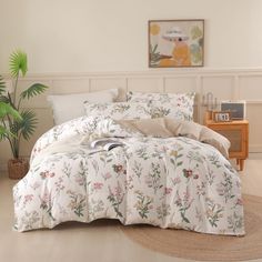 a bed with white and pink flowers on it in a room next to a potted plant