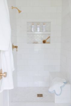 a bathroom with white tile and gold faucet shower head, soap dispenser on the wall