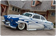 an old car with flames painted on it's hood parked in front of a house