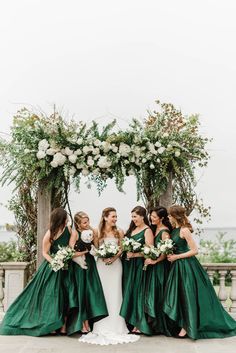 the bride and her bridesmaids pose for a photo in front of an arch decorated with greenery