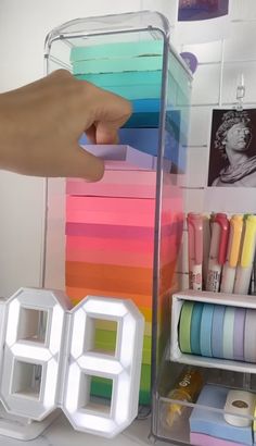 a person's hand is reaching for the number eighty on a stack of colored sticky notes