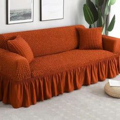 an orange couch in a white room with two pictures on the wall and a potted plant next to it