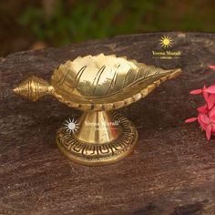 a small brass vase sitting on top of a wooden table next to some pink flowers