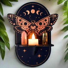 a candle is lit in front of a butterfly shaped wall clock with the moon and stars on it