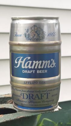 a can of beer sitting on top of a wooden table next to a building and grass