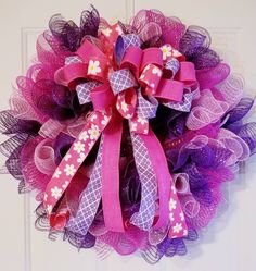 a purple and pink mesh wreath with flowers on the front door, hanging on a white door