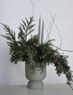 a green vase filled with greenery and candles