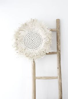 a large white flower hanging from the side of a wooden ladder next to a wall