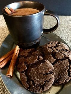 two chocolate cookies and cinnamon sticks on a plate next to a cup of hot cocoa