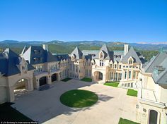 an aerial view of a large mansion in the middle of a field with mountains in the background