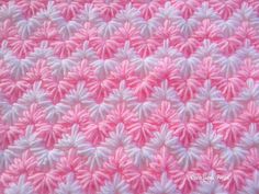 a pink and white crocheted blanket with small flowers on the bottom, in rows