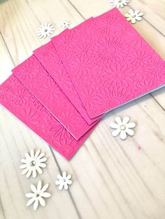 three pink cards with white daisies on the table next to them and some paper flowers