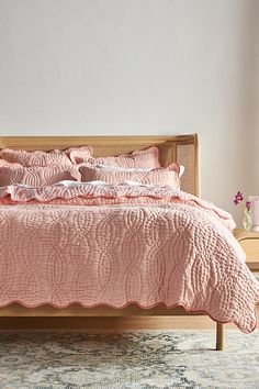 a bed with pink comforter and pillows in a white room next to a window