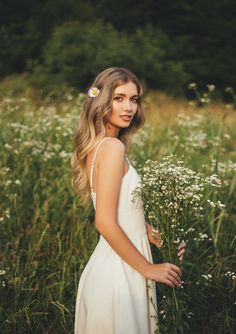 a woman in a white dress is standing in a field with wildflowers and grass