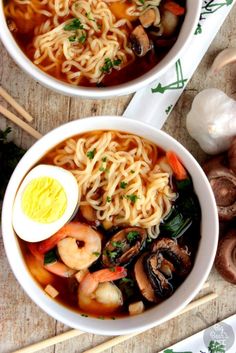 two bowls filled with noodles and vegetables on top of a wooden table next to chopsticks