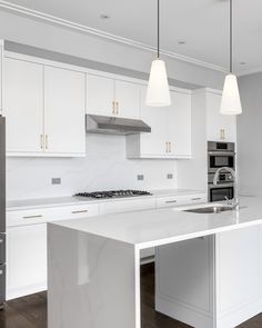 a kitchen with white cabinets and marble counter tops, two pendant lights over the island