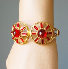 "This gorgeous bracelet features two large red glass cabochon stones surrounded by emerald cut red stones and set in gold-tone metal. This unusual bracelet has an art moderne look and dates to the 1940s. It has a spring hinge on the back that is in great working order. I don't see a maker's mark on this piece, but it is well-made. The interior width is 2-3/8\" and the setting at the front is 1.25\" tall. The interior circumference is 6.5\". This bracelet is in wonderful condition and looks strik Vintage Cabochon Bangle Bracelets, Red Adjustable Vintage Cuff Bracelet, Vintage Collectible Cuff Bracelet With Polished Finish, Vintage Cabochon Cuff Bangle, Silver Vintage Cabochon Cuff Bracelet, Red Stones, Spring Hinge, Red Stone, Maker's Mark