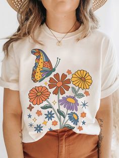 a woman wearing a hat and t - shirt with colorful flowers on the front, while she is holding her hands in her pockets