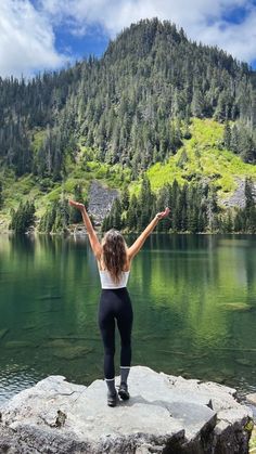 a woman standing on top of a rock next to a lake with her arms in the air