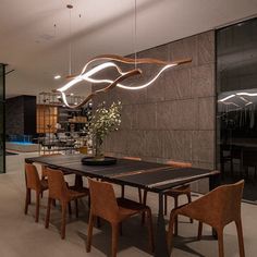 a dining room table with chairs and lights hanging from it's ceiling, in front of a glass wall