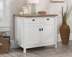 a white sideboard with two drawers and a lamp next to it on a hard wood floor