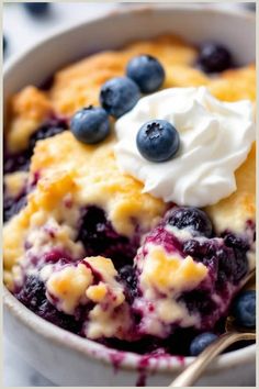 Blueberry cobbler topped with whipped cream and fresh blueberries in a bowl.