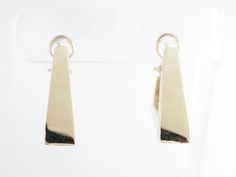 These fancy modern dangle earrings are finished in 14 karat yellow gold. They are secured by an omega closure and face forward for a good view of the triangle design from the side view. The triangles have lovely open spaces at the closure, existing as a design element as well as a functional space for wearing them.Composition: 14 Karat Yellow GoldGeneral Characteristics:Measurements: 1.5 inches x 8.19 mmTotal Gram Weight: 19.6Era: Modern 1970-PresentInscription: 14 KT--ALL PIECES ARE SUBJECT TO Contemporary Yellow Gold Hoop Earrings For Formal Occasions, Contemporary Yellow Gold Hoop Earrings, Modern Pierced Huggie Earrings For Formal Occasions, Modern Yellow Gold Dangle Huggie Earrings, Contemporary Sterling Silver Earrings In Yellow Gold, Contemporary Sterling Silver Yellow Gold Earrings, Contemporary Yellow Gold Sterling Silver Earrings, Modern 14k Gold Rectangular Earrings, Modern 14k Gold Clip-on Earrings