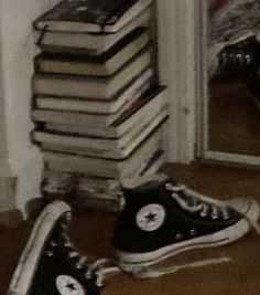 a stack of books sitting next to a pair of black converses on the floor