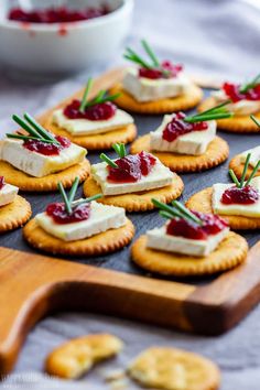 crackers with cranberry sauce and cheese on them are arranged on a wooden board