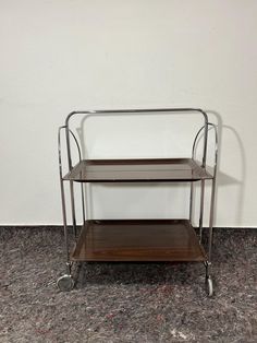 two tiered metal and wood serving cart with wheels on the bottom, against a white wall