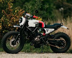 a white and red motorcycle parked on the side of a road next to tall grass