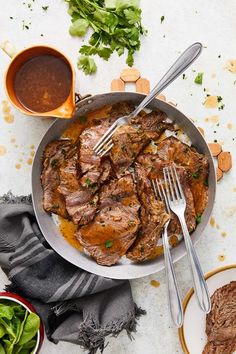 a pan filled with meat and vegetables on top of a white counter next to sauce