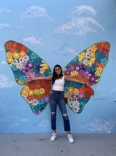 a woman standing in front of a wall with a butterfly painted on it's wings