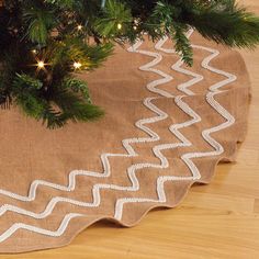 a christmas tree skirt is on the floor next to a fir tree with lights in the background