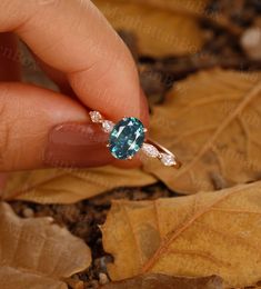 a woman's hand holding an engagement ring with a blue topazte surrounded by leaves