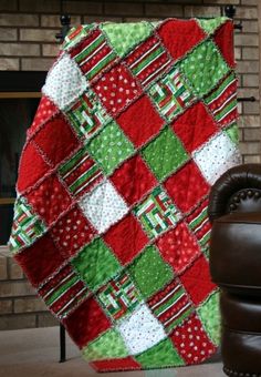 a red, green and white quilt sitting on top of a chair next to a fireplace